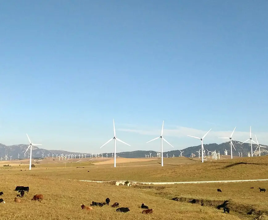 Bergige Landschaft mit mehreren Windrädern unter blauem Himmel.