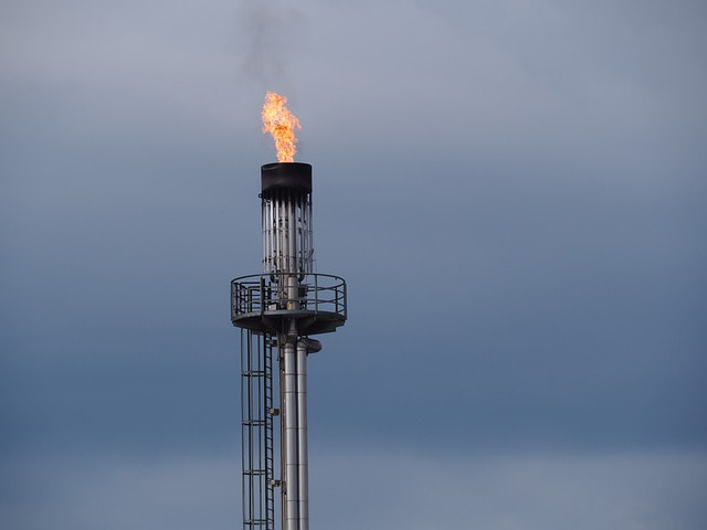 Gasflamme am Ende eines hohen Stahlrohres vor grauem Himmel