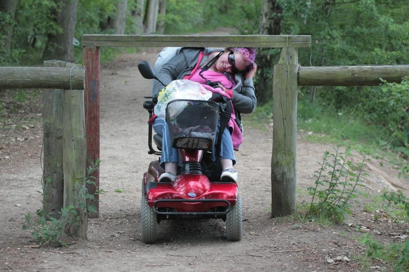 Frau im Rollstuhl fährt unter einer Absperrung durch
